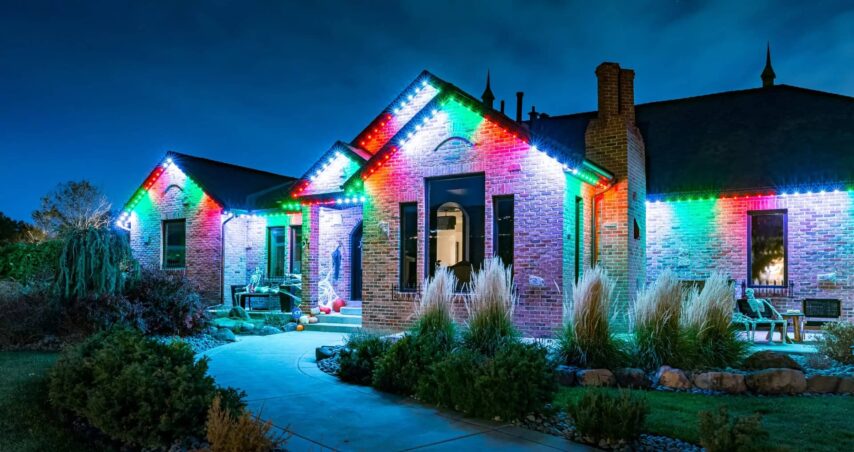 Attached image file A brick house at night is decorated with colorful Christmas lights along the roofline, illuminating the walkway and garden plants in front of the home. The festive atmosphere is enhanced by a professional trimlight installation, ensuring the house lights shine beautifully throughout the holiday season.